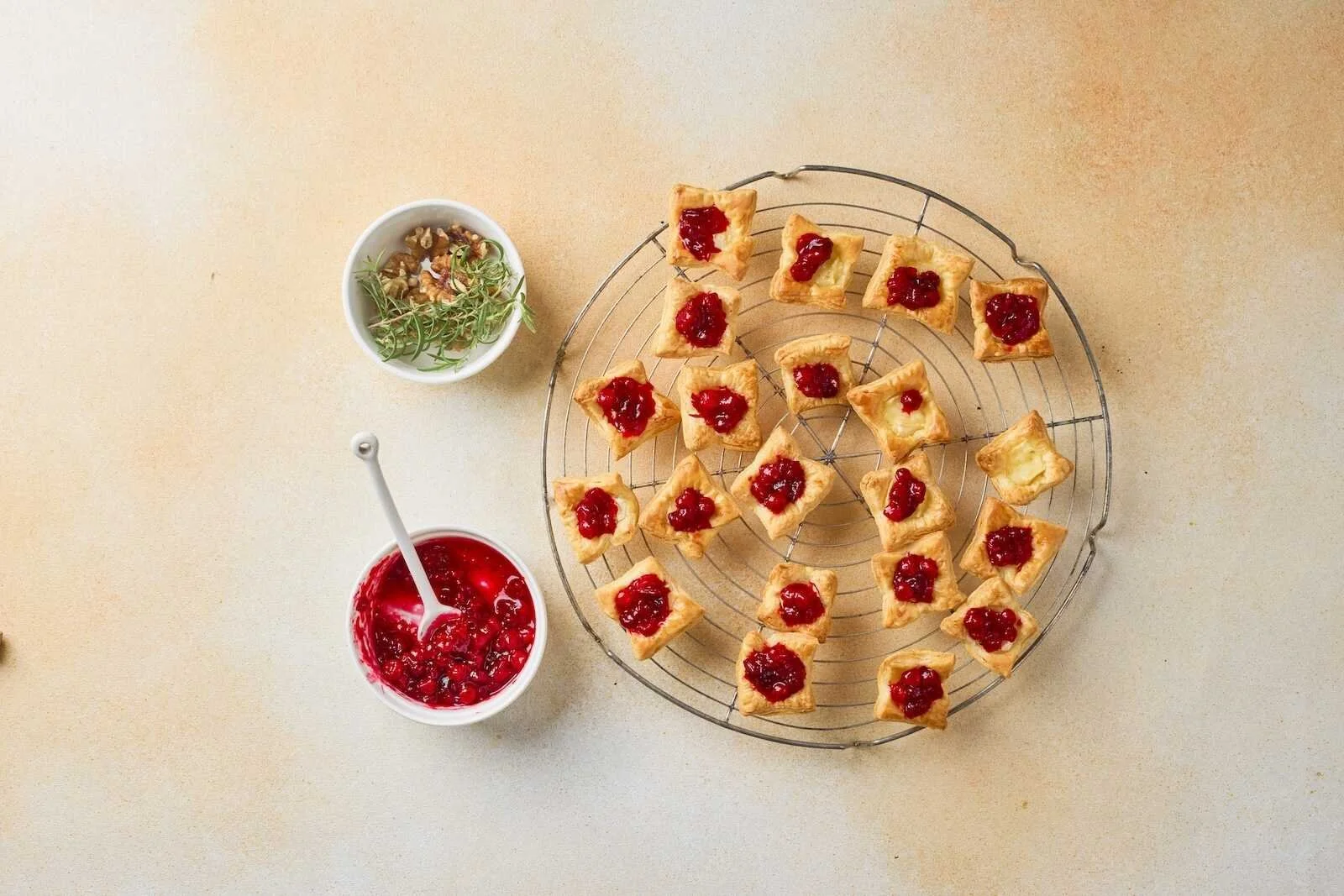 Holiday Heaven Bites topped with homemade cranberry sauce while cooling on a wire rack, ready for walnuts and fresh rosemary garnish.