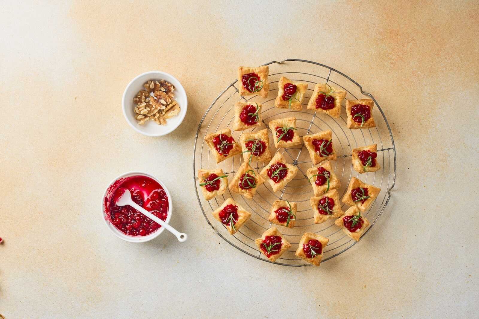Holiday Heaven Bites topped with homemade cranberry sauce and fresh rosemary, cooling on a wire rack before being finished with chopped walnuts.