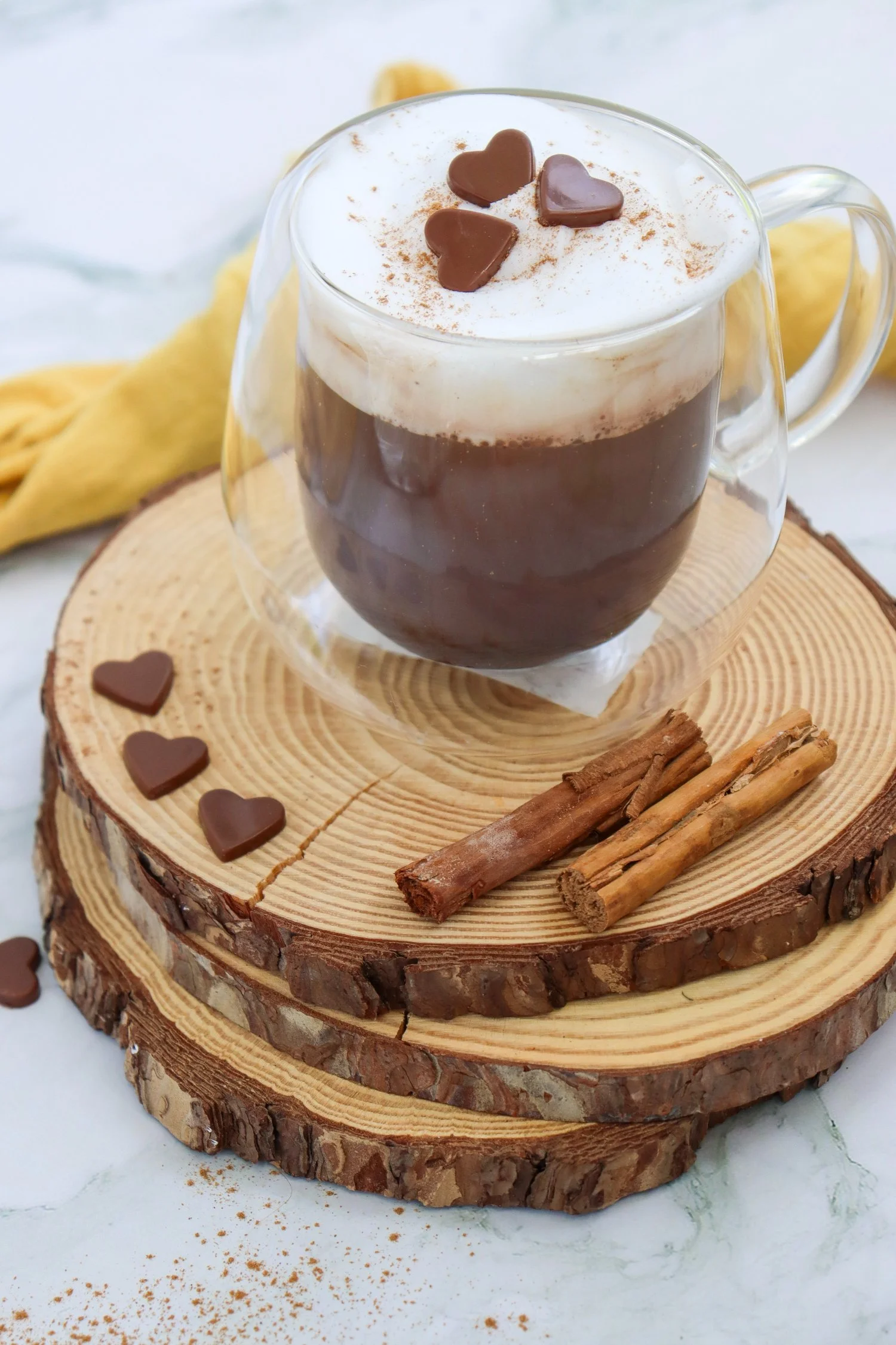 Pumpkin Spice Hot Chocolate topped with creamy foam, pumpkin pie spice, and chocolate hearts, served with cinnamon sticks for a cozy fall treat.