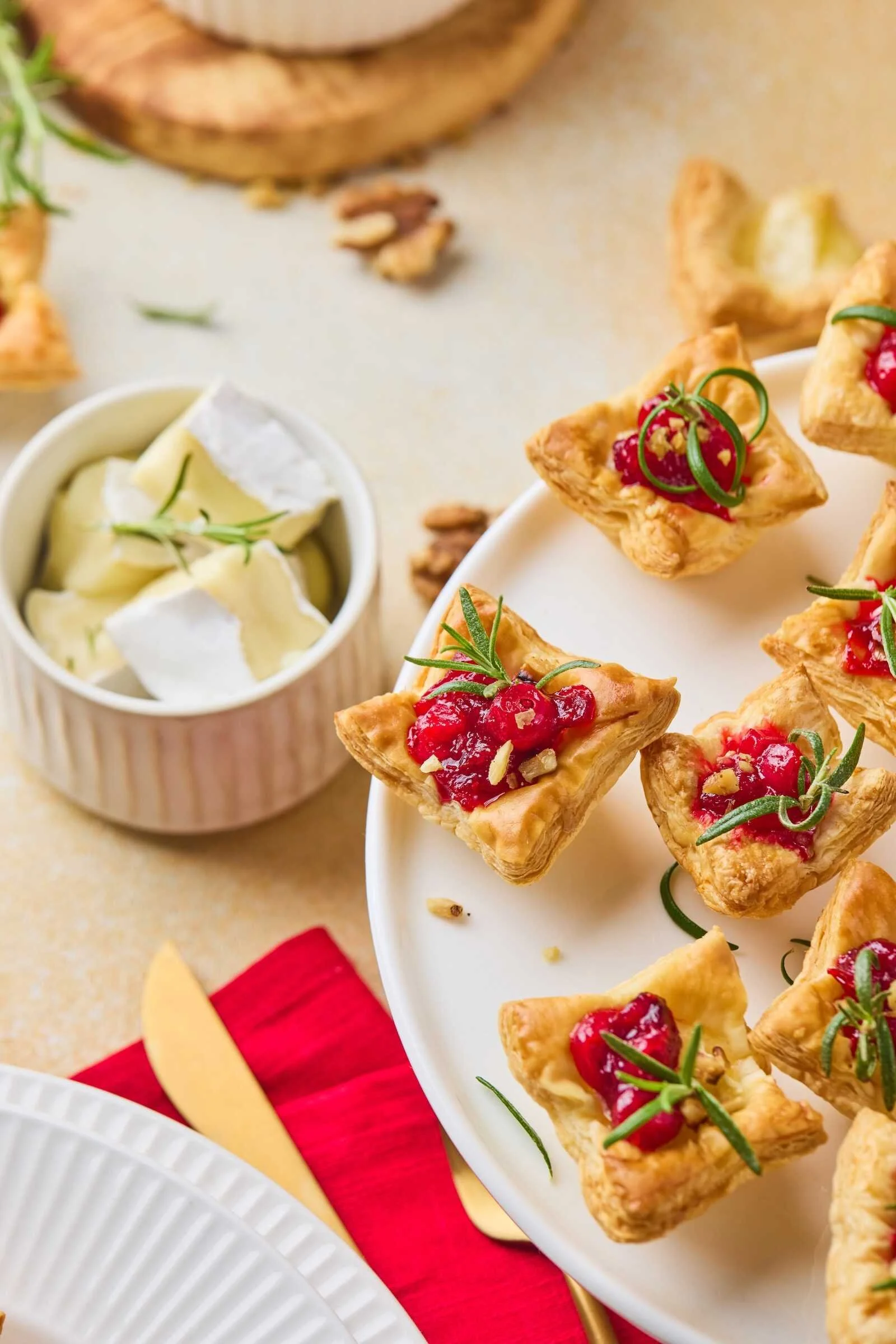 Close-up of Holiday Heaven Bites with flaky puff pastry, creamy Brie cheese, homemade cranberry topping, chopped walnuts, and fresh rosemary on a festive serving platter.