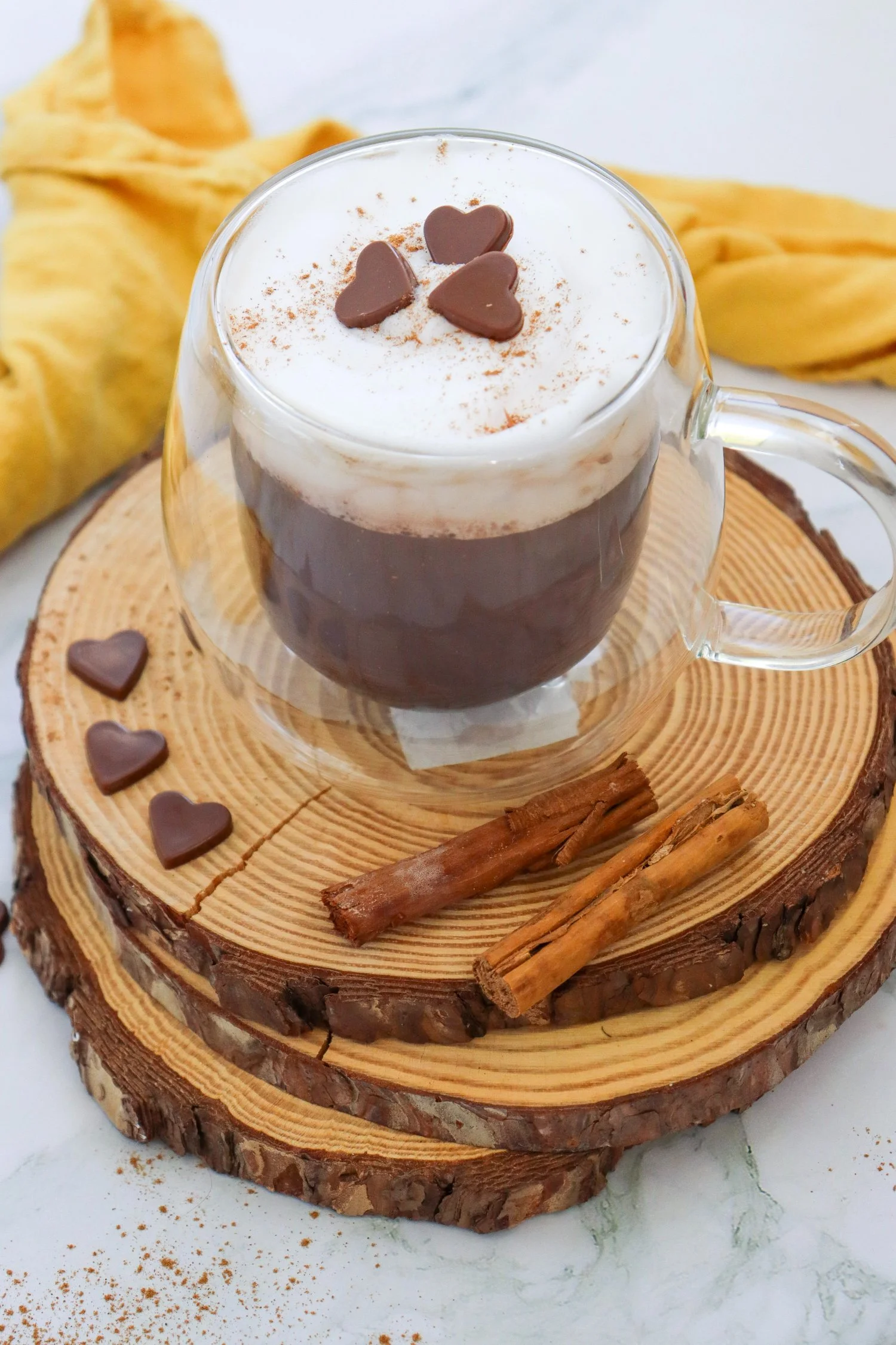 Pumpkin Spice Hot Chocolate topped with creamy foam, cinnamon spice, and heart-shaped chocolates, served with cinnamon sticks.