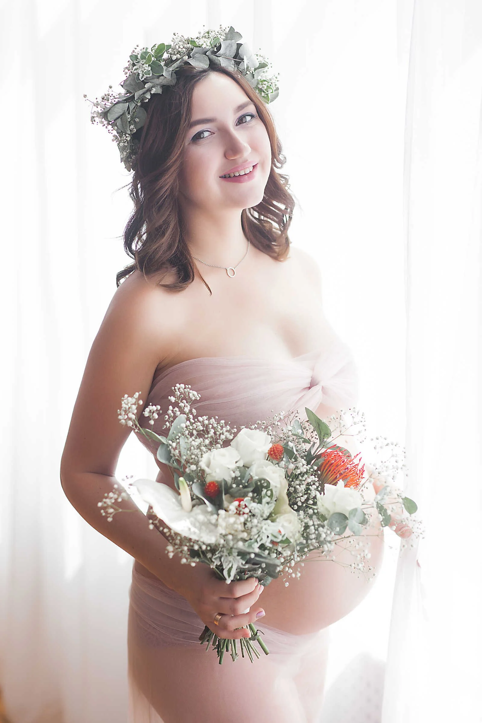 Nude maternity photos portrait of pregnant woman with floral crown holding bouquet in soft natural window light