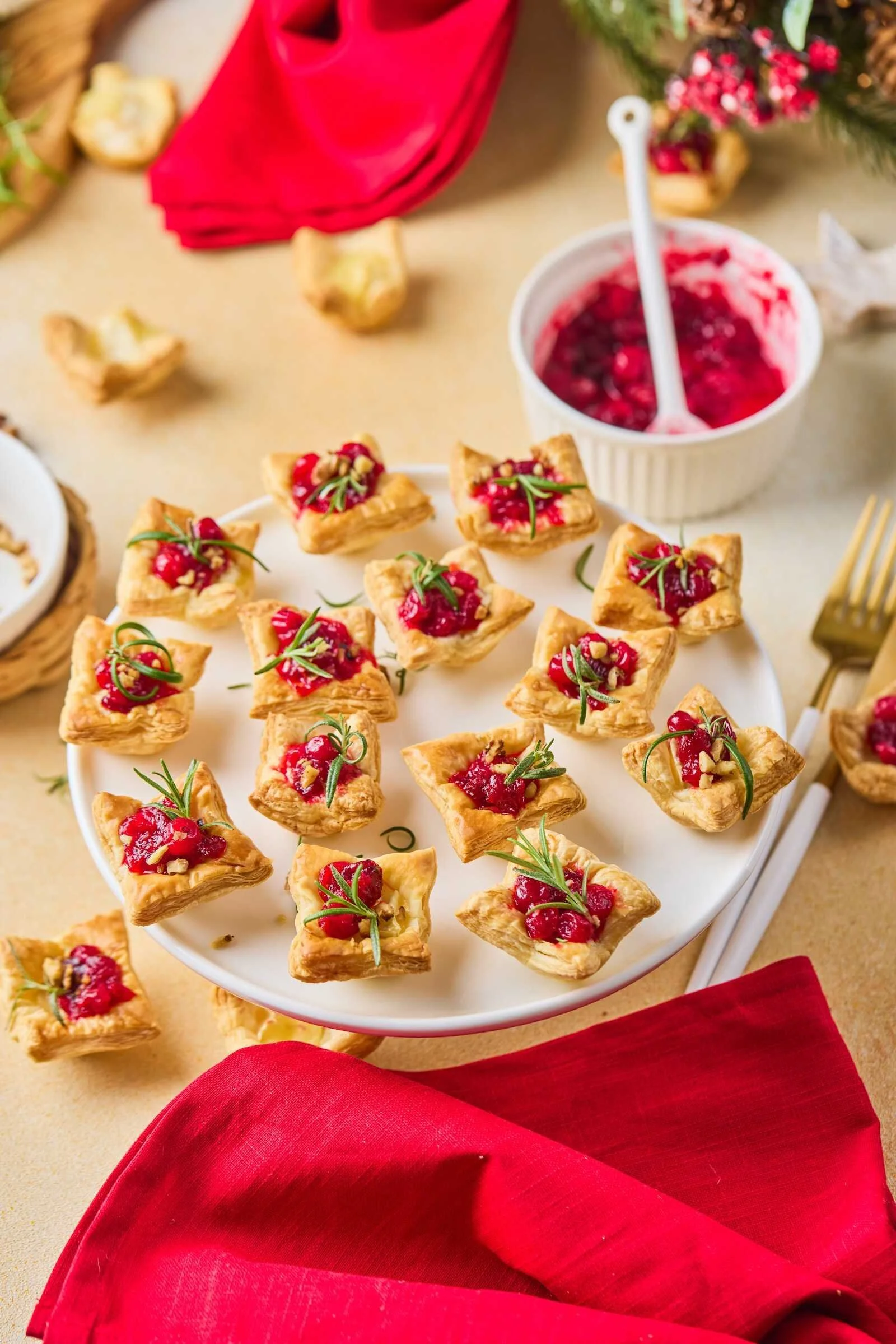 Holiday Heaven Bites arranged on a serving platter with flaky puff pastry, creamy Brie cheese, homemade cranberry topping, chopped walnuts, and fresh rosemary for a festive holiday appetizer.