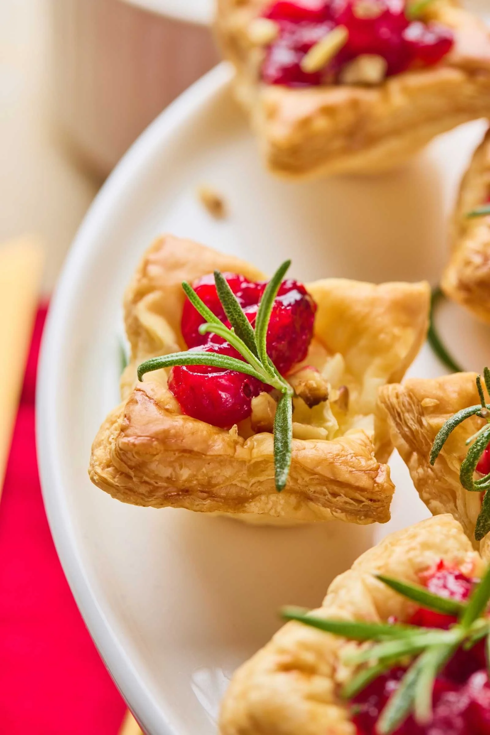 Close-up of a Holiday Heaven Bite with flaky puff pastry, creamy Brie cheese, cranberry topping, chopped walnuts, and fresh rosemary garnish.
