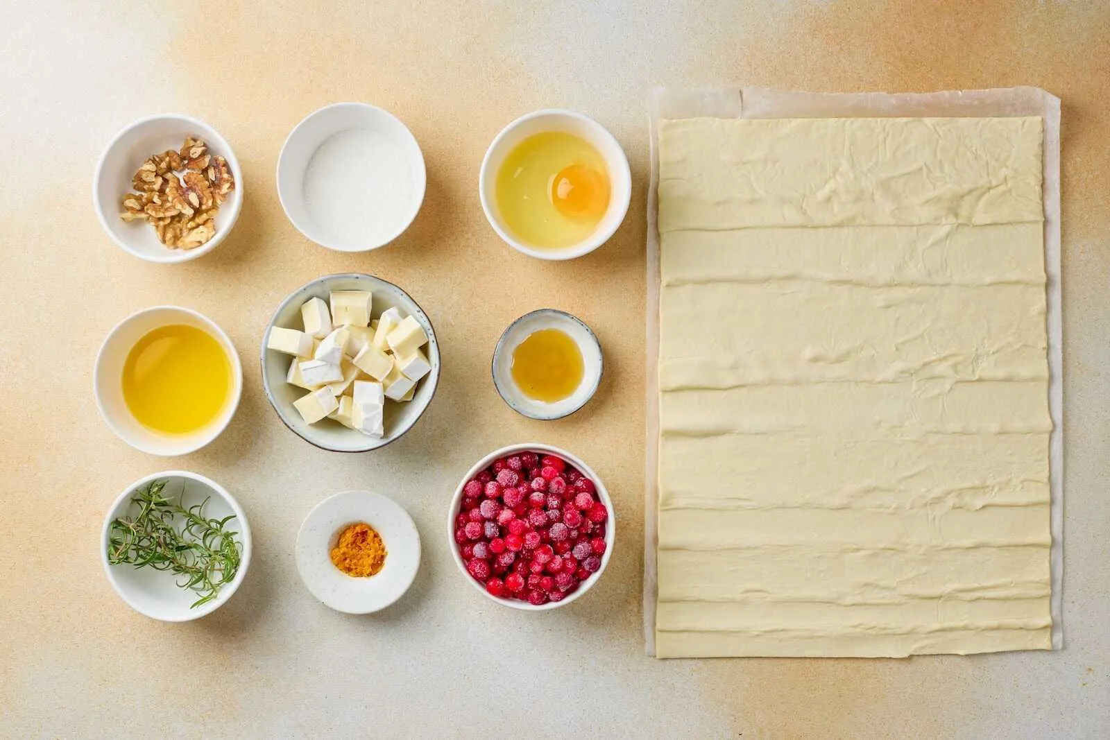 Ingredients for Holiday Heaven Bites including puff pastry, Brie cheese, fresh cranberries, egg, orange zest, honey, rosemary, walnuts, and butter arranged for an easy holiday appetizer recipe.