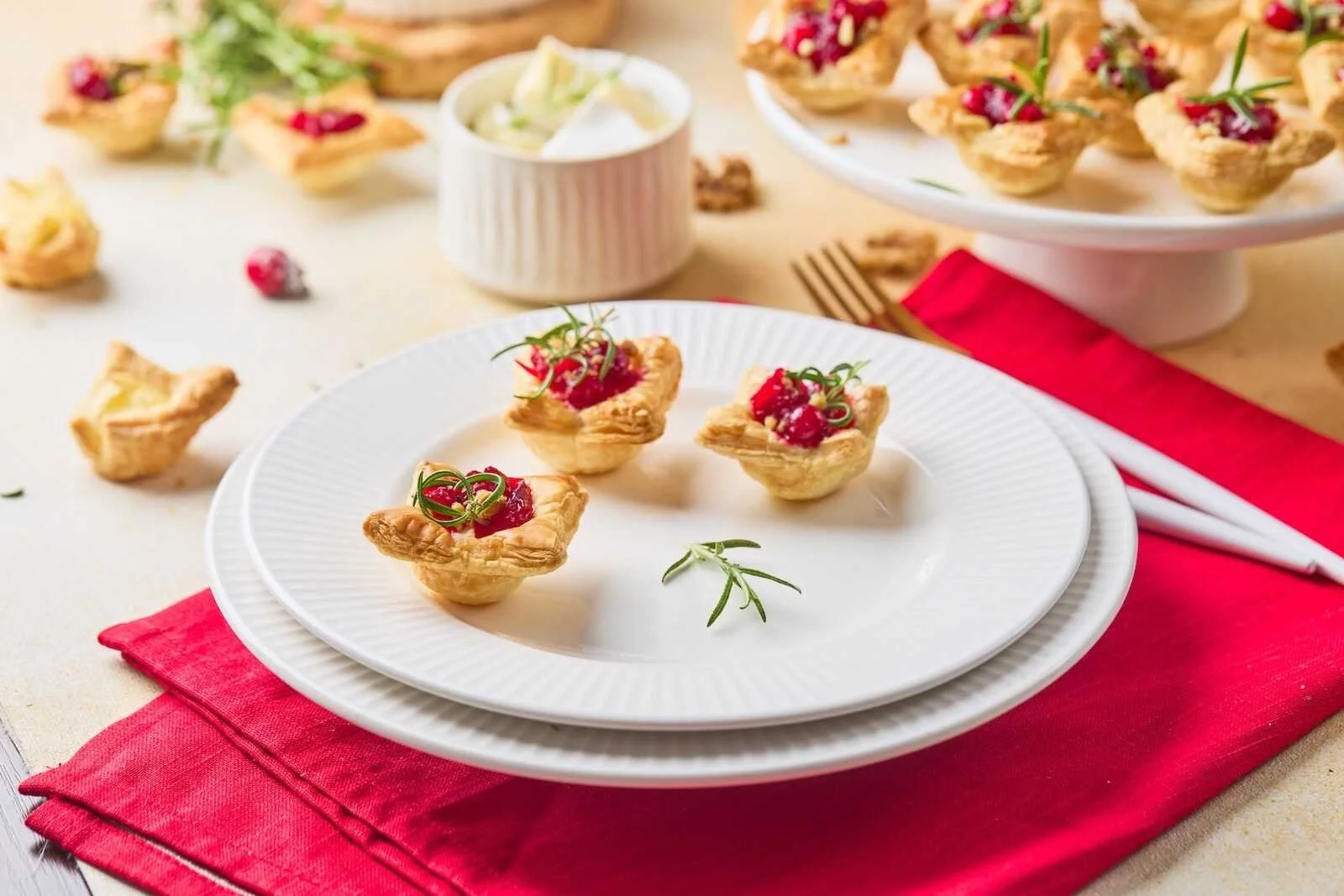 Holiday Heaven Bites served on a white plate with flaky puff pastry, creamy Brie cheese, homemade cranberry topping, and fresh rosemary for an elegant holiday appetizer.