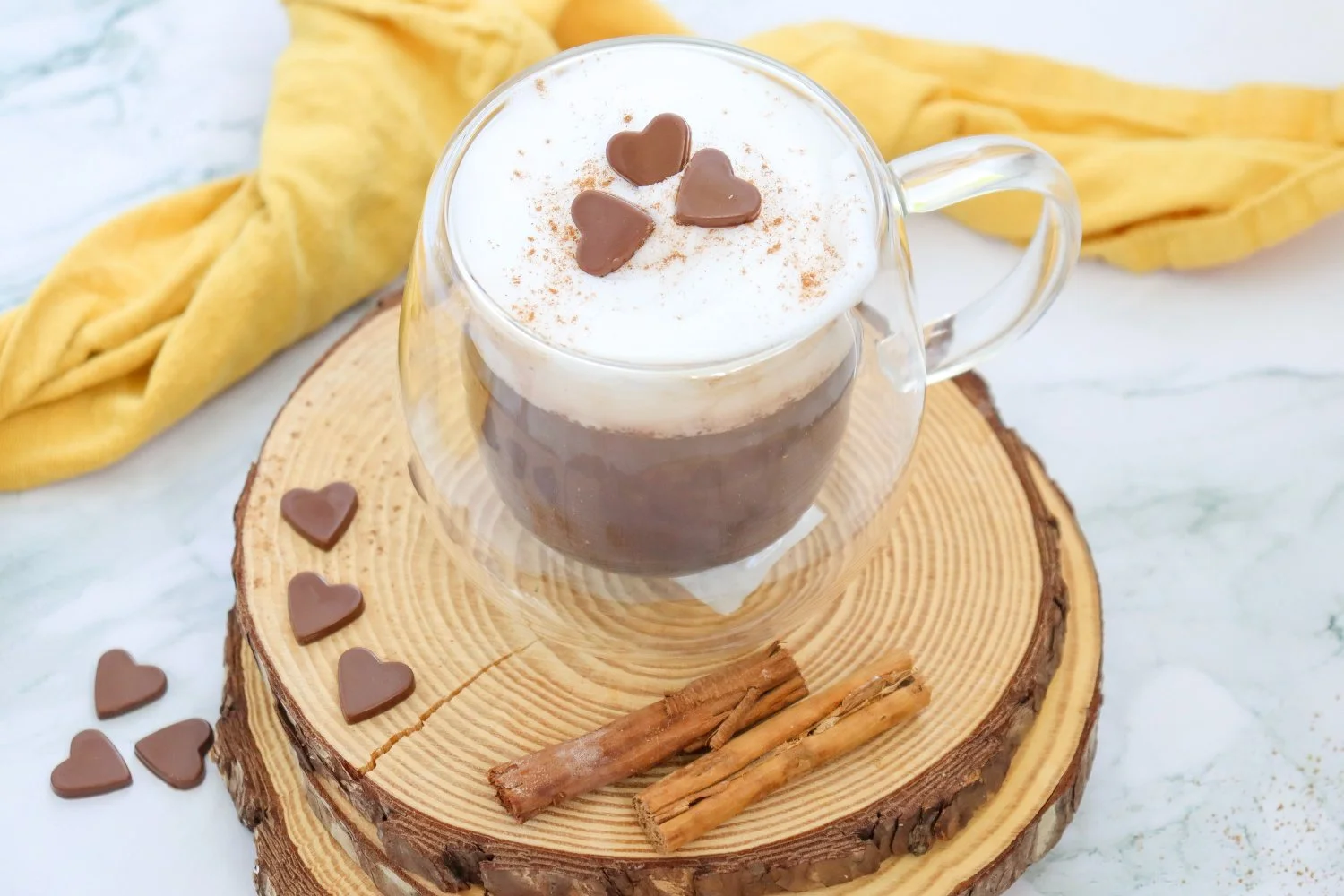 Pumpkin Spice Hot Chocolate topped with creamy whipped foam, cinnamon, and heart-shaped chocolates in a clear glass mug.