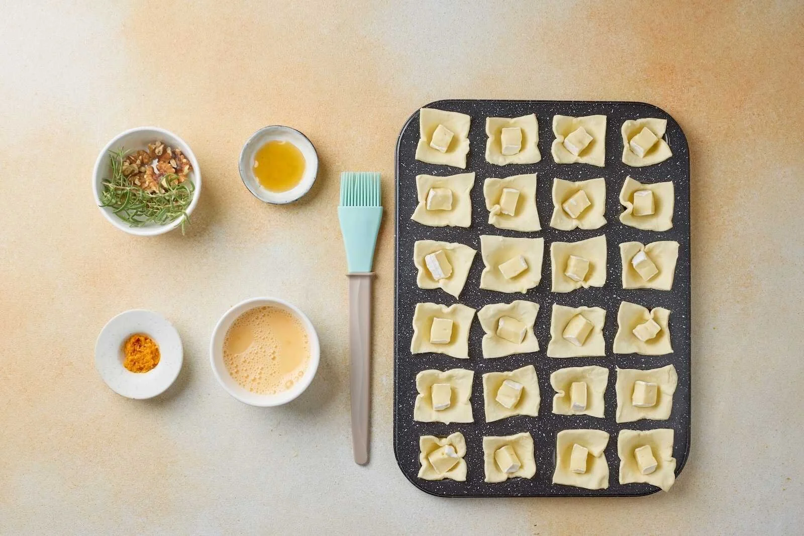 Holiday Heaven Bites before baking with puff pastry cups filled with Brie cheese, brushed with egg wash, and prepared in a mini muffin pan.