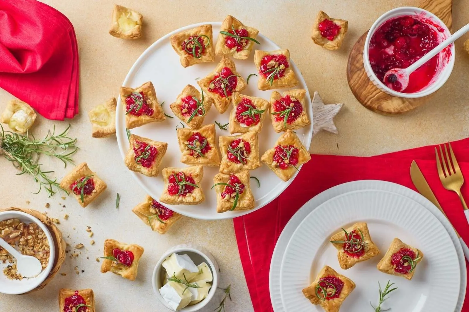 Overhead view of Holiday Heaven Bites with flaky puff pastry, creamy Brie cheese, homemade cranberry topping, chopped walnuts, and fresh rosemary served on festive holiday plates.