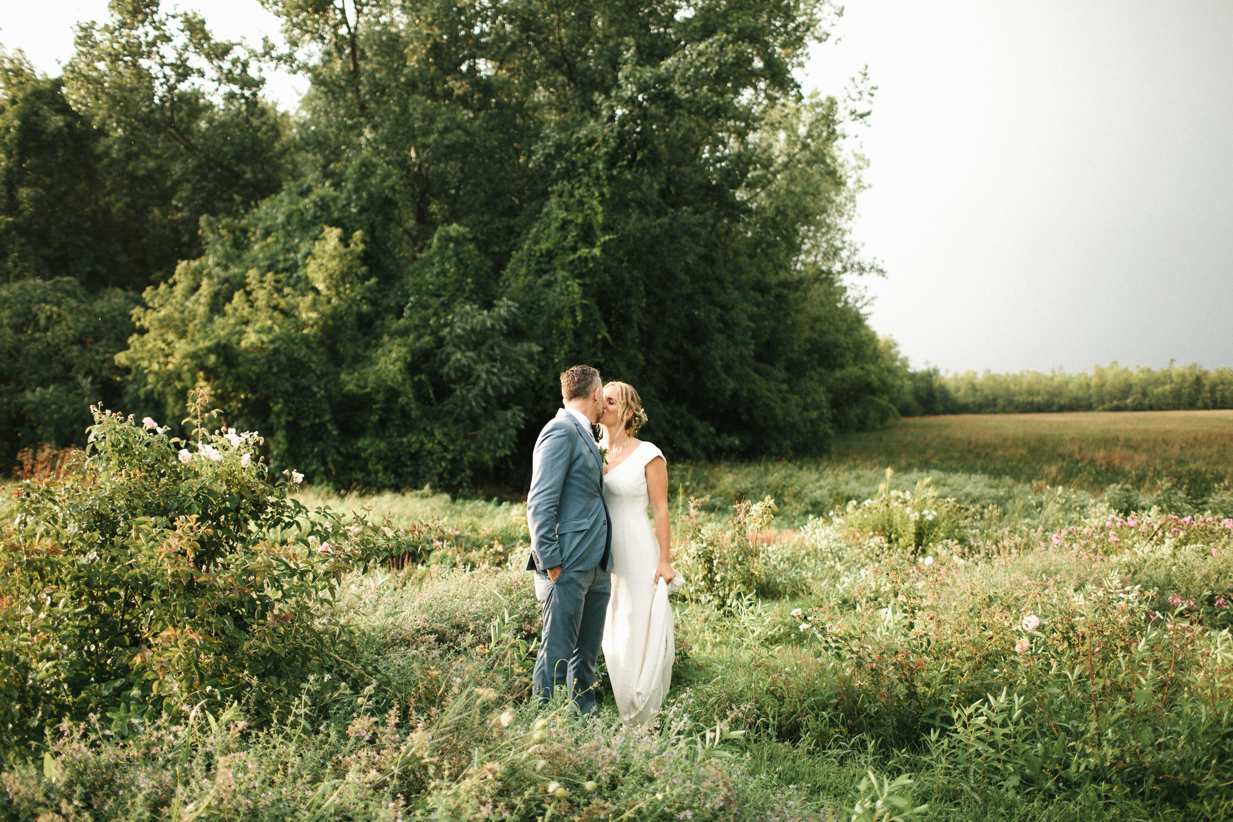  Bride and groom kiss in flower field during sunset. 