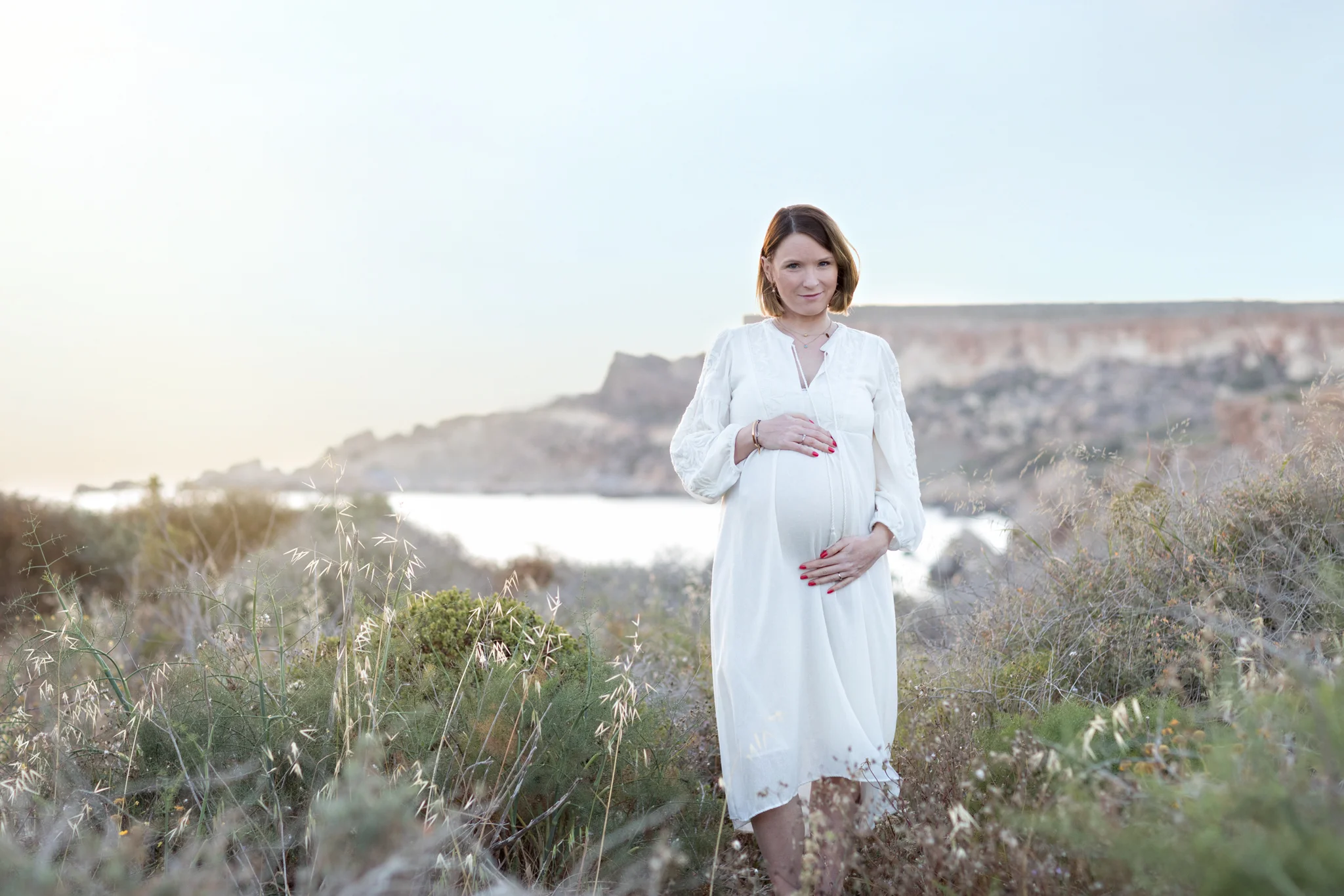 expecting, boho maternity dress, content, longing, Mediterranean sea, backlight, sunset, mountains, polish in malta, maternity photo shoot malta, natural light, outdoor photo shoot