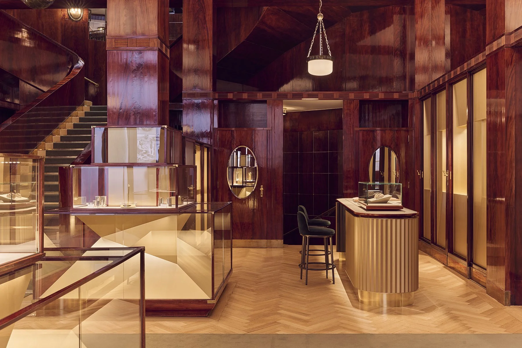 Elegant retail store interior with dark polished wood walls, glass display cases, a curved staircase, and modern lighting fixtures.