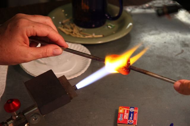 A metal punty is applied to each end and the glass is heated as Heather prepares to pull and twist.