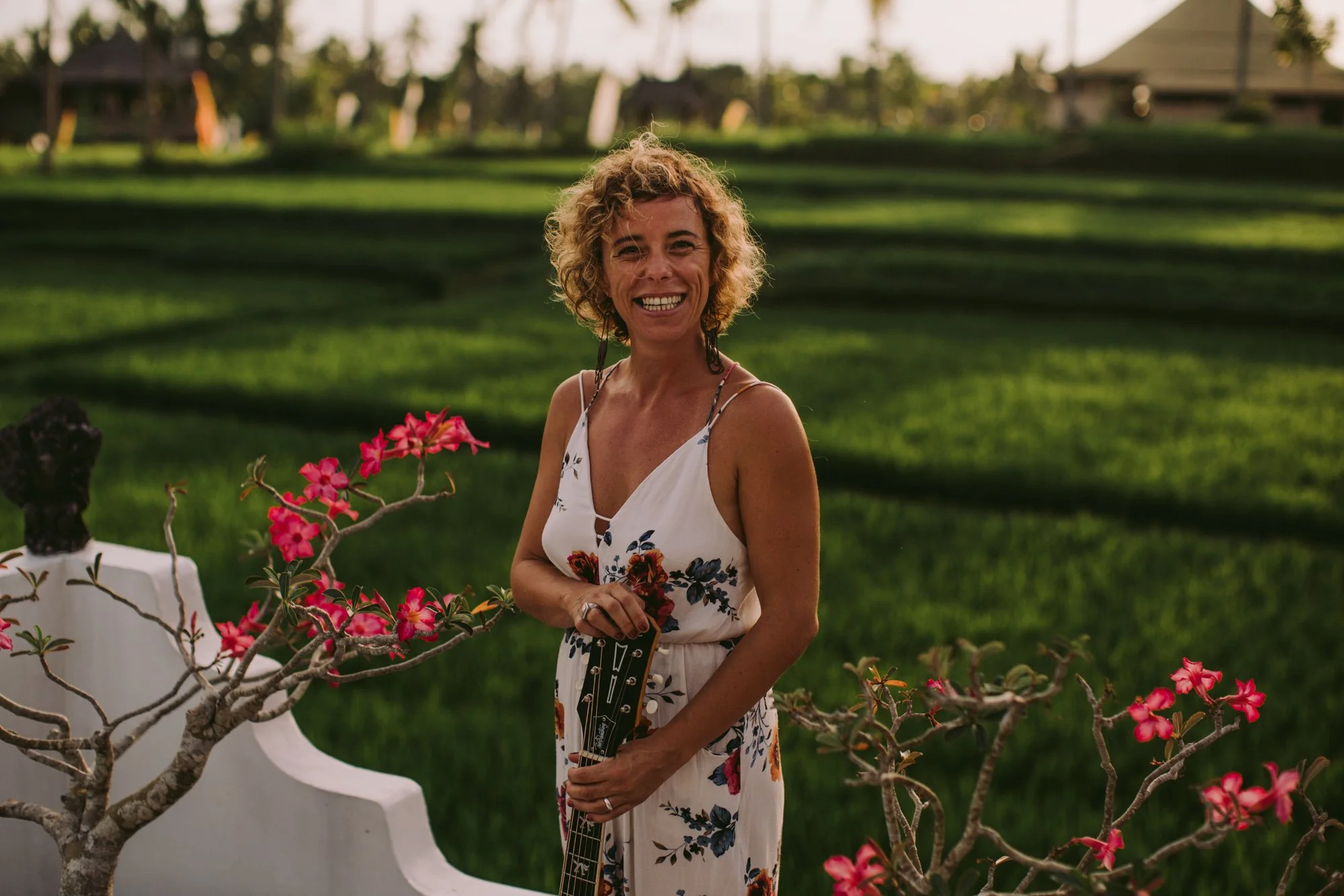 A musician at an outdoor venue, holding her guitar, and smiling.