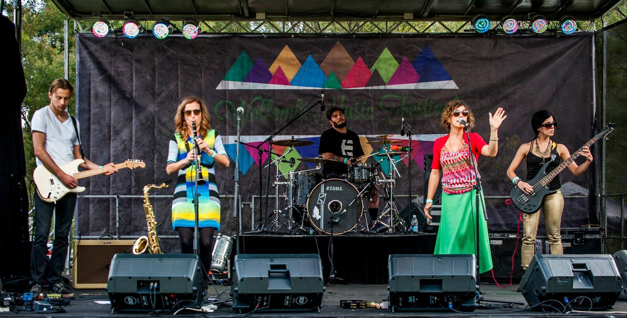 A live reggae band performing on an outdoor stage at a music festival with musicians playing instruments and singing.