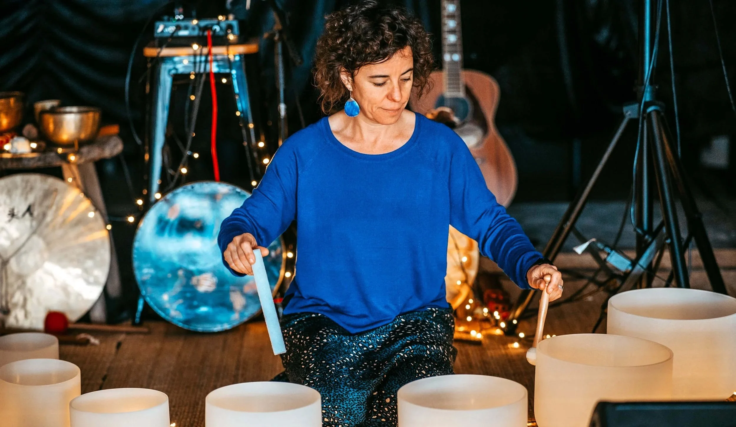 Sound healing facilitator playing crystal singing bowls in a studio with musical instruments during a sound bath session.