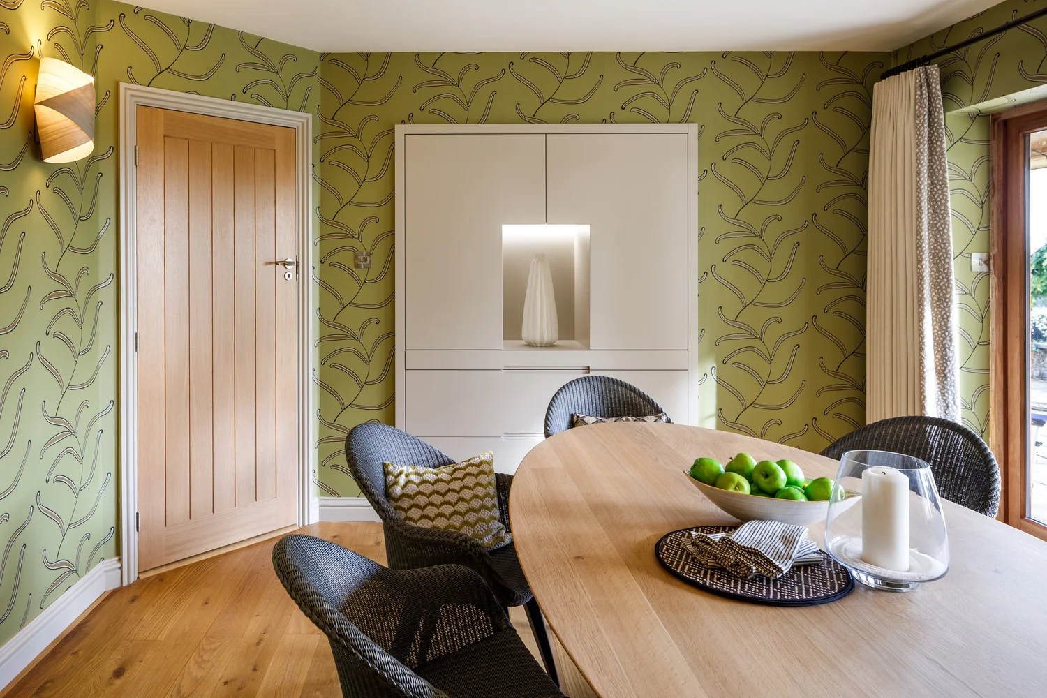 Dining room with olive green botanical wallpaper and oak table in a Mid Devon home designed by Michelle Sucksmith