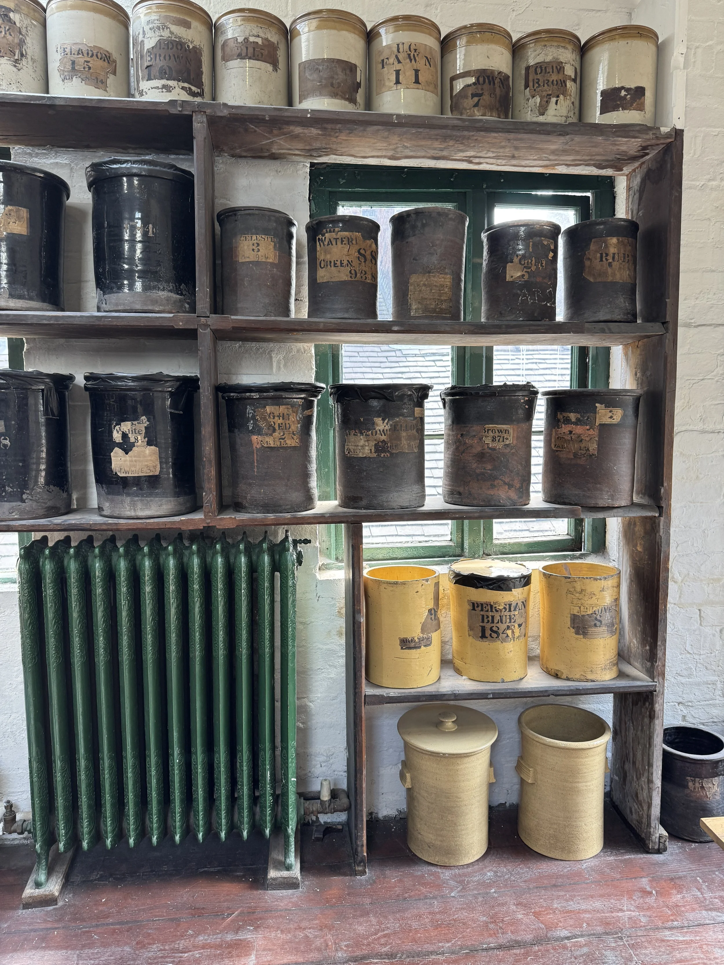 Shelves of labelled glaze jars beside a green cast iron radiator, Gladstone Pottery Museum