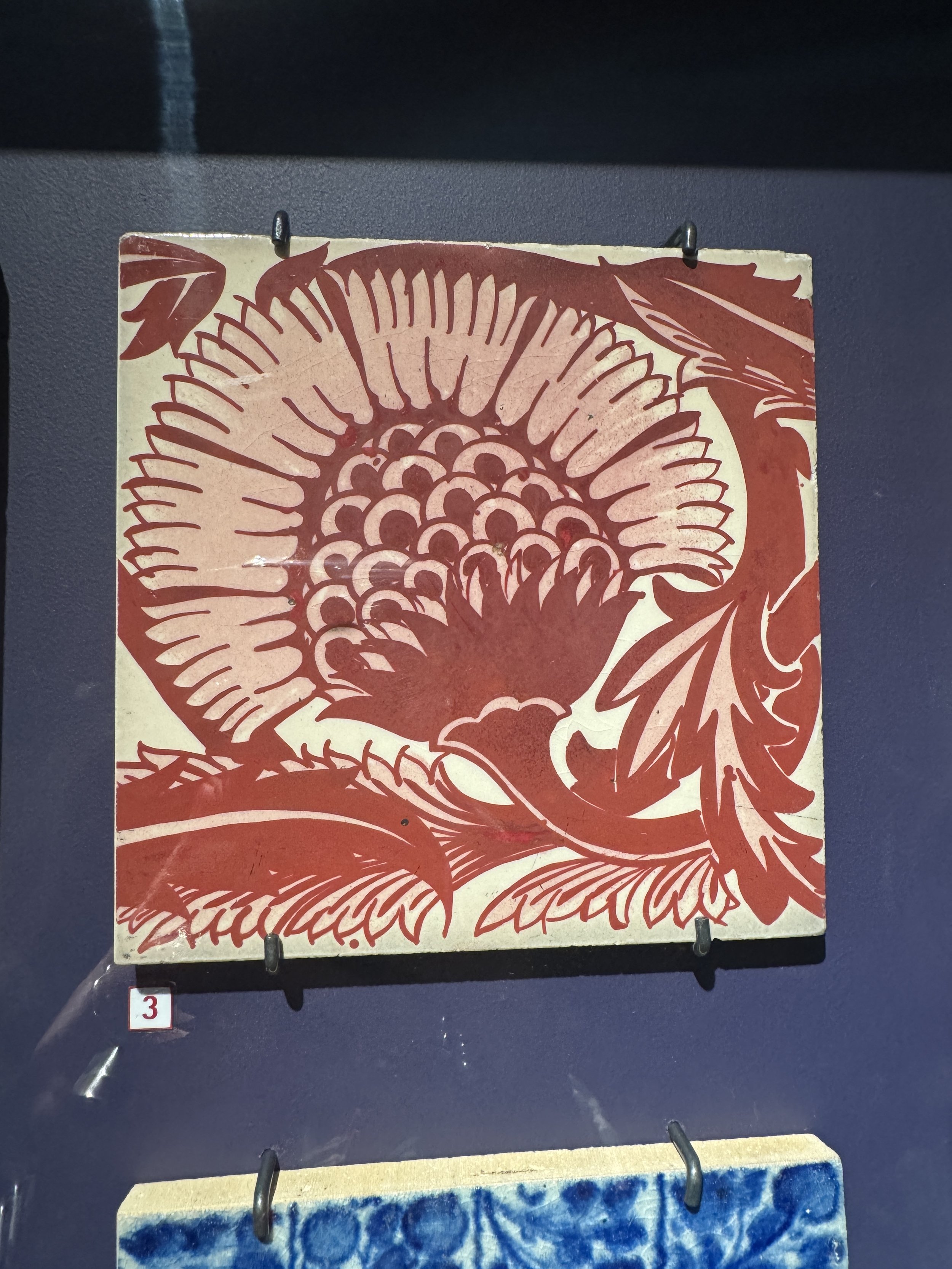 Red and white Arts and Crafts style tile with a stylised flower, Gladstone Pottery Museum