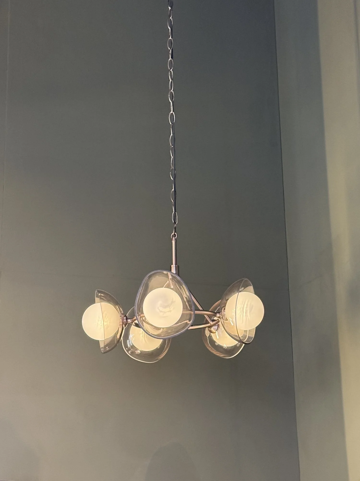 A pendant light with five glass globes hanging against a grey green wall, Industville at Decorex 2026