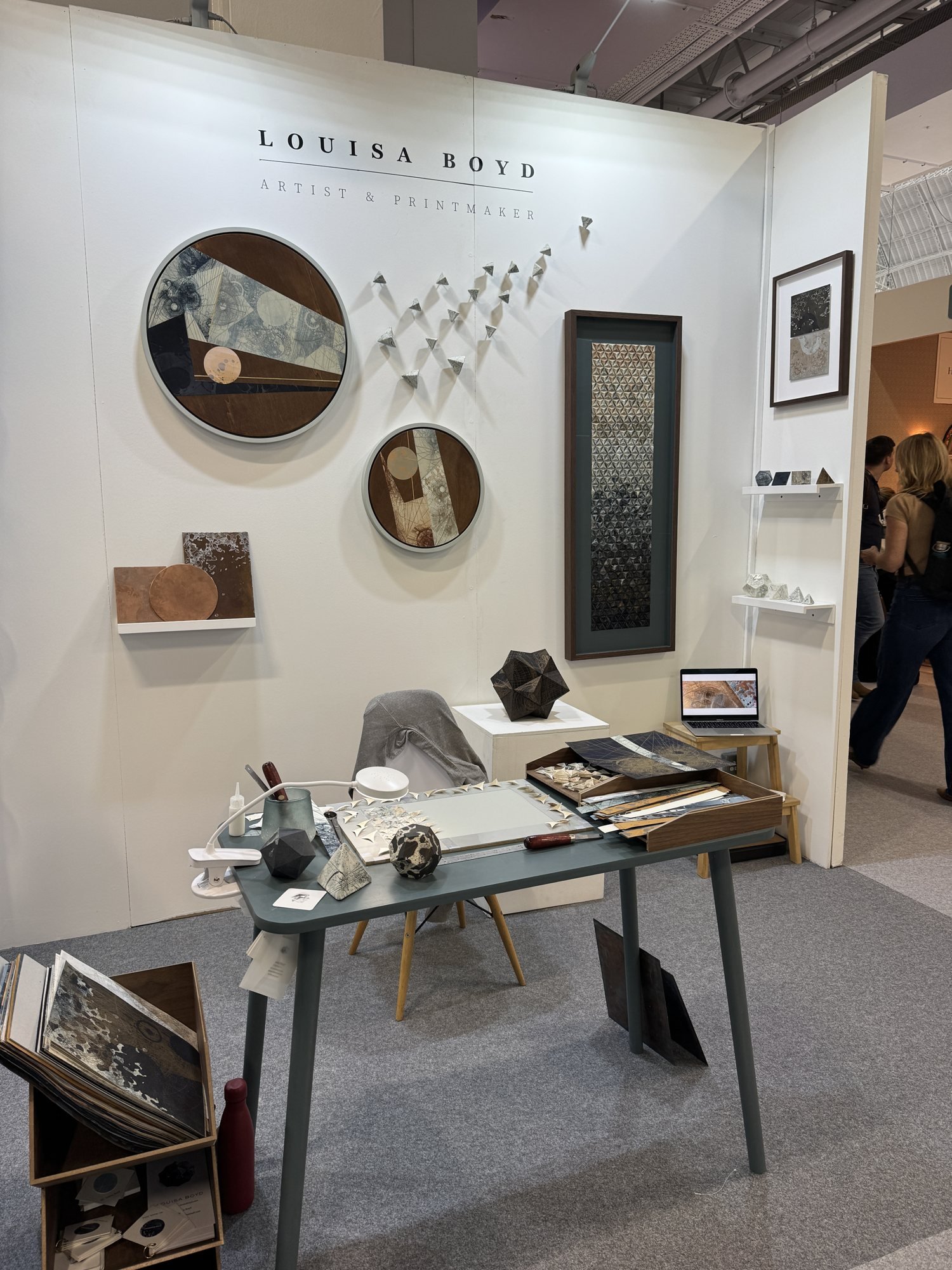 A white stand with circular framed artworks and small folded paper sculptures on the wall, Louisa Boyd in Making Spaces at Decorex 2026