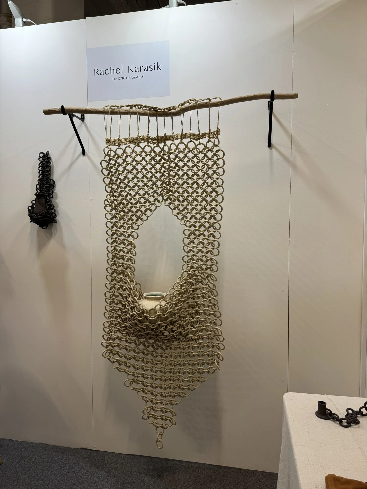 A long hanging of interlinked natural clay rings suspended from a branch on a white wall, Rachel Karasik in Making Spaces at Decorex 2026