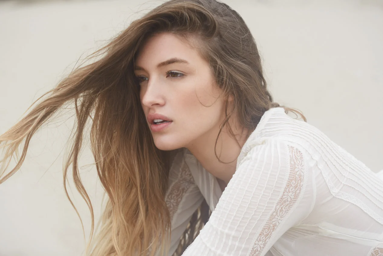 Female fashion model laying in the sand photographed at Cannon Beach Oregon. She is wearing a white dress. Beachy hair is whipped by the wind.