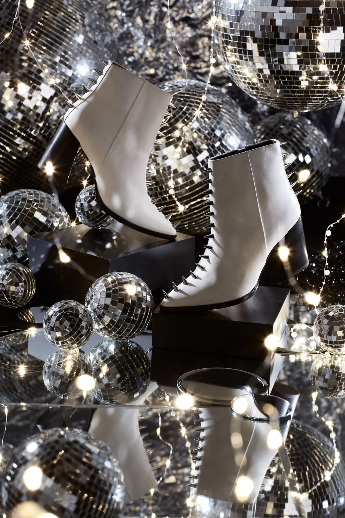  Shoe Party! Holiday accessory disco party scene. White ankle boots with a chunky black heel and silver spikes outlining the shape by Top Shop. Shot nestled in a chaotic jumble of mirrors, twinkle lights and disco balls. Photography: Leah Perry Photo
