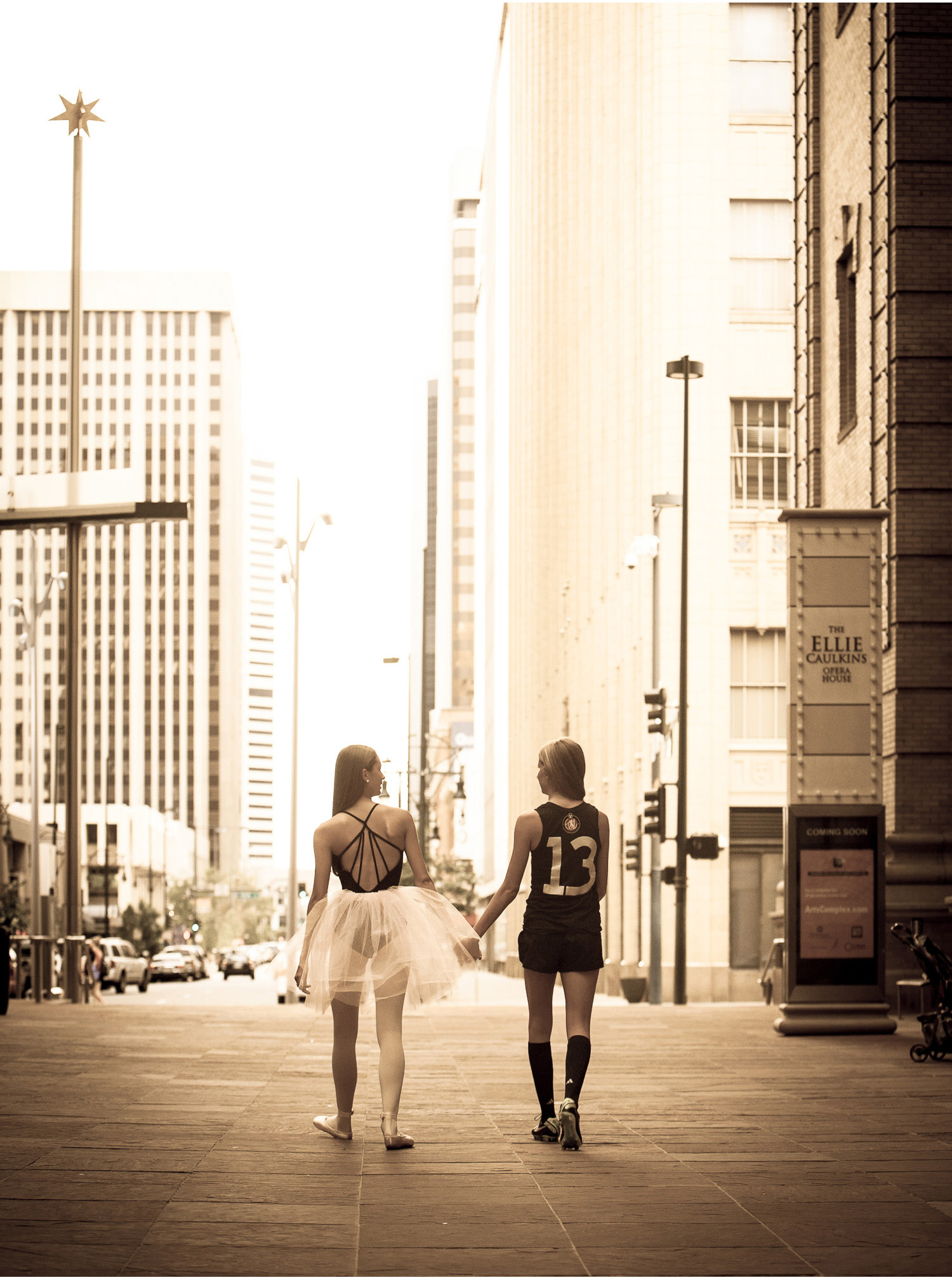 Best friends walk holding hands and walk out of the Denver Center for Performing Arts during their high school senior portrait session with photographer Jennifer Koskinen, Merritt Portrait Studio.