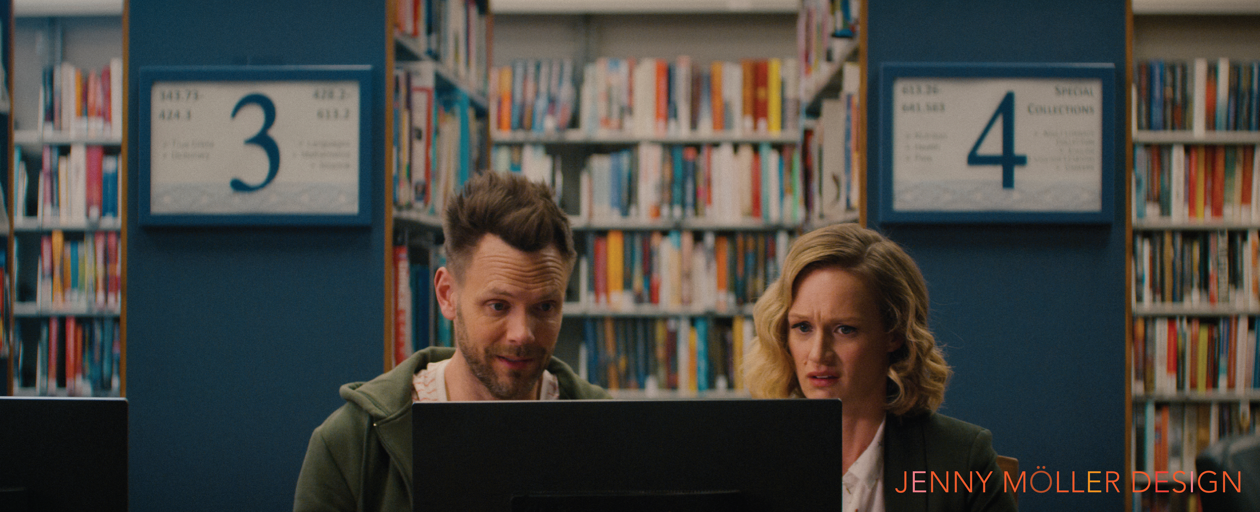 A man and woman sitting at computers in a library, looking confused. Behind them, shelves with books and signs indicating sections 3 and 4.