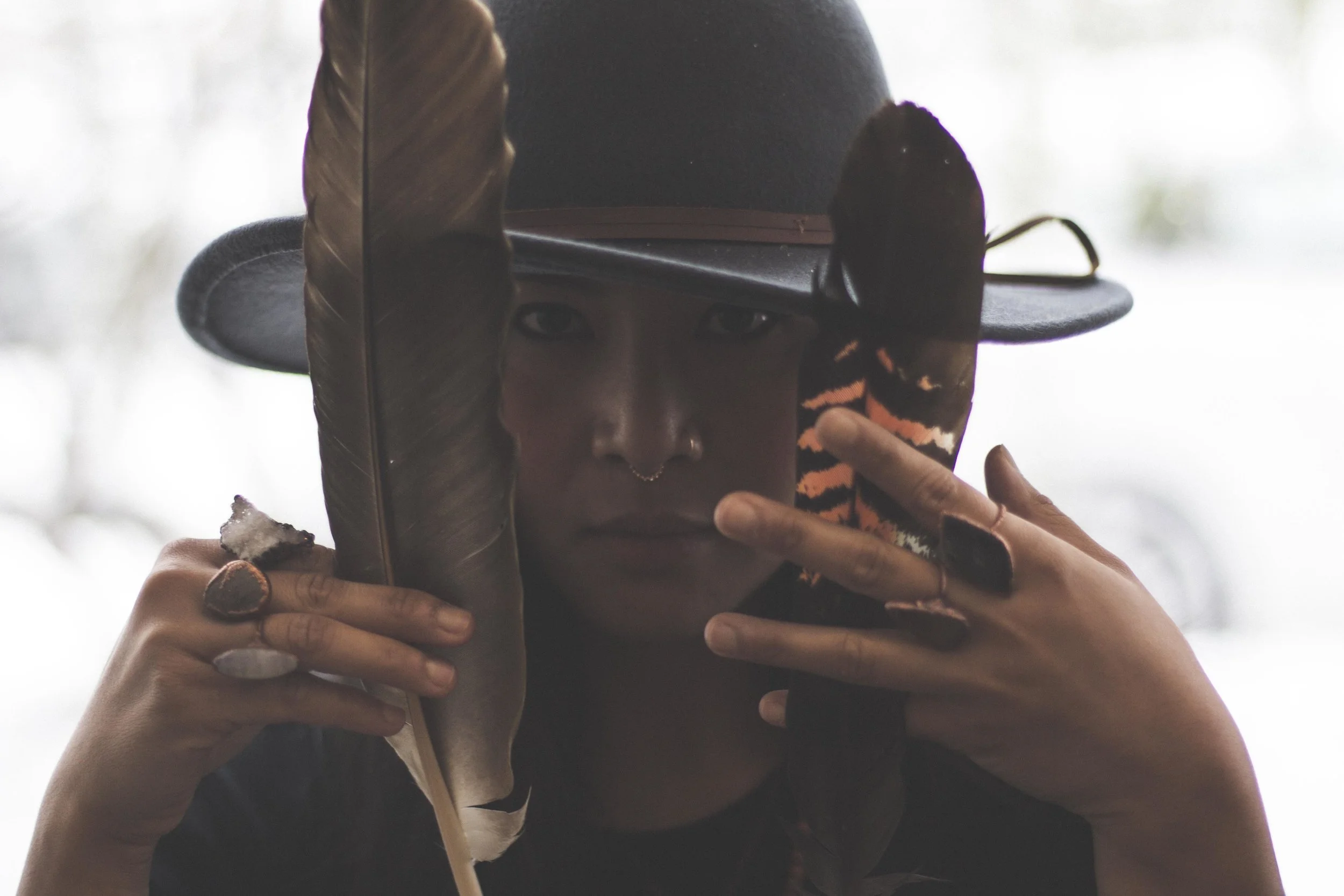 Woman wearing handmade crystal jewellery with feathers in her hand and hat on her head