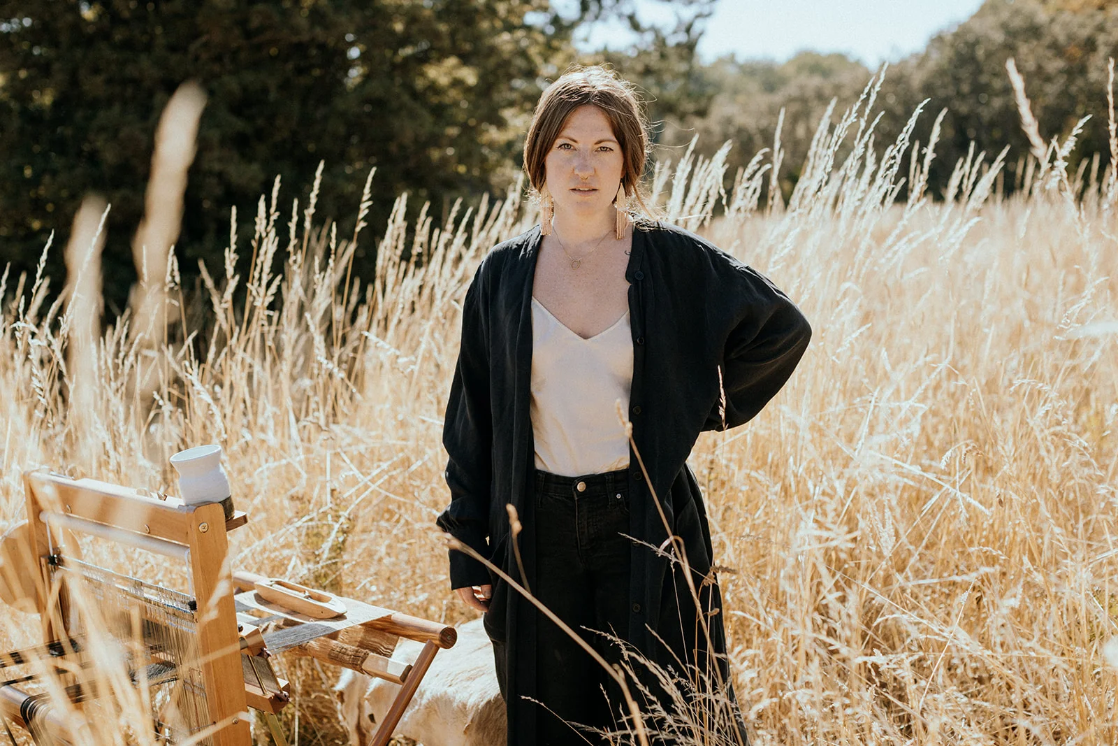 Woman standing next to loom in a field of tall grass