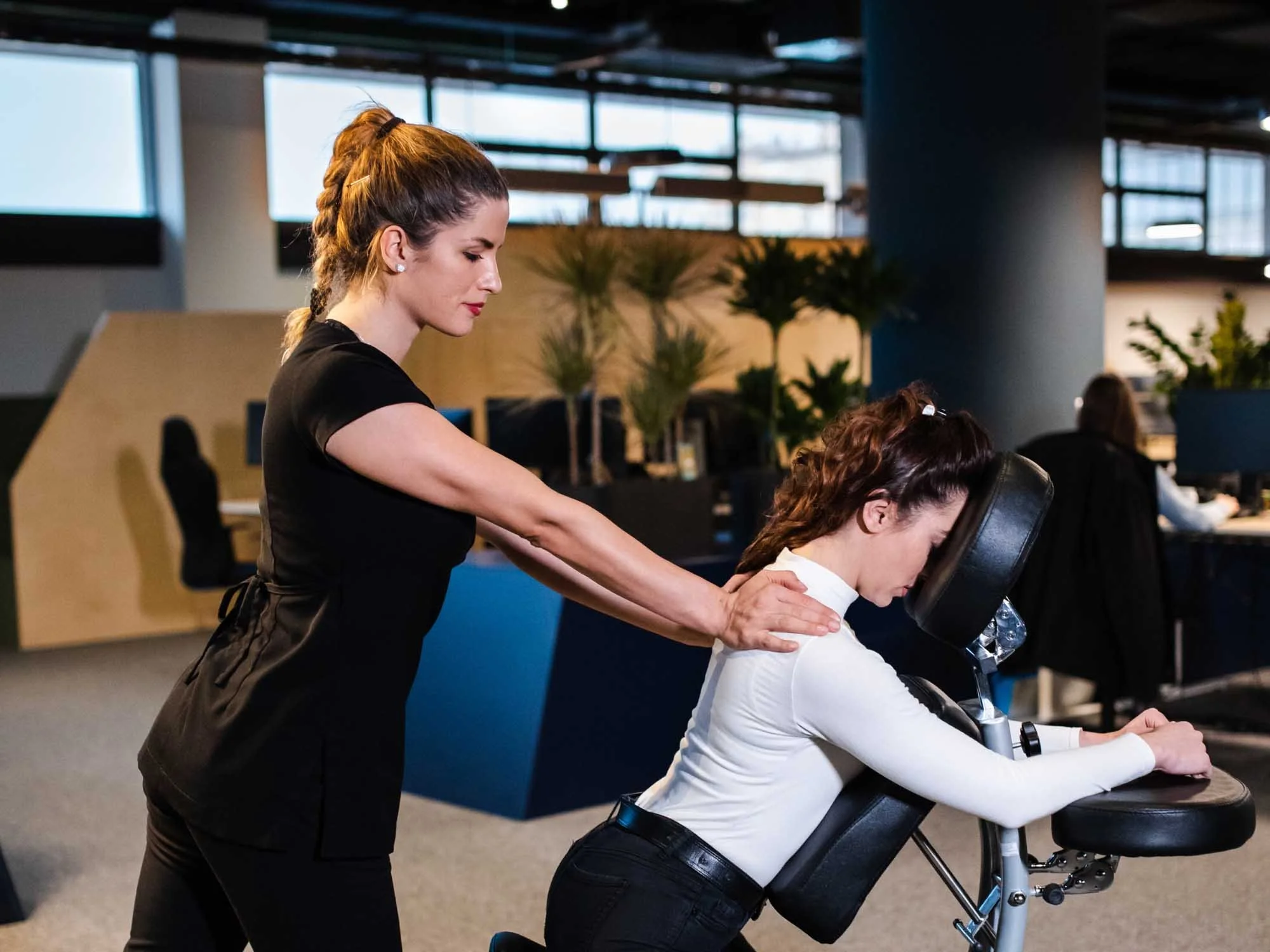 Massage therapist providing seated chair massage during a corporate workplace wellness event.