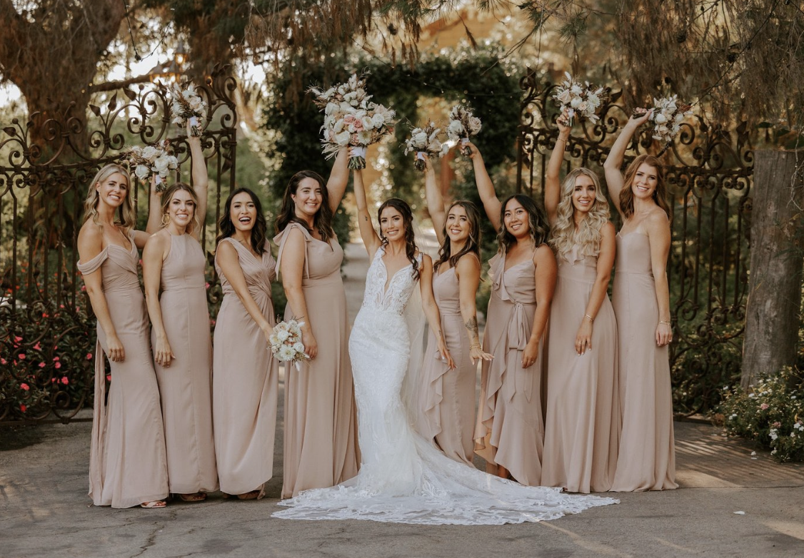 Bride standing with her bridal party in coordinated blush dresses at an outdoor wedding.