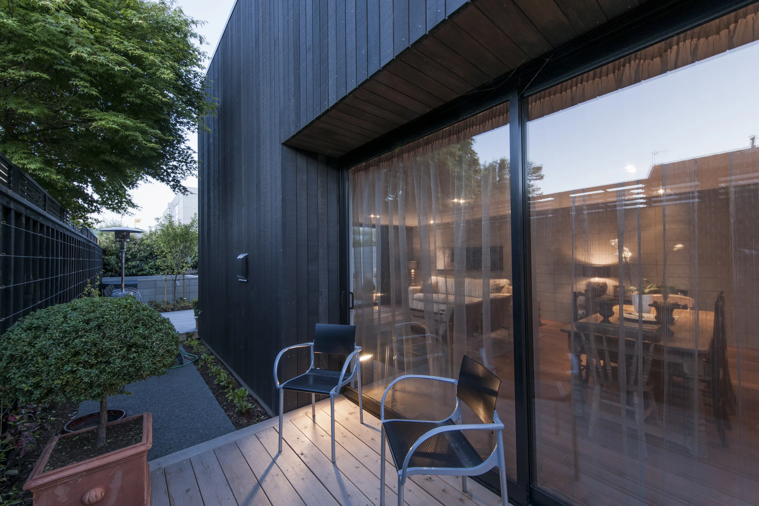 Conference Street This structure was designed as two houses, for two separate clients with two completely different briefs. In profile, the two homes share an inter-tenancy wall and take on two major forms from the street. The first form contains the single-story double garage. The second sits over the garage and cantilevers out towards the street. To achieve privacy and the intention of an industrial aesthetic the homes are clad in black cedar and concrete block with darkened powder-coated matte steel mesh louvers over the street facing façade. The interiors include a black steel kitchen with concrete bench top, concrete and cedar walls softened by way of a bleached oak floor and soft furnishings.