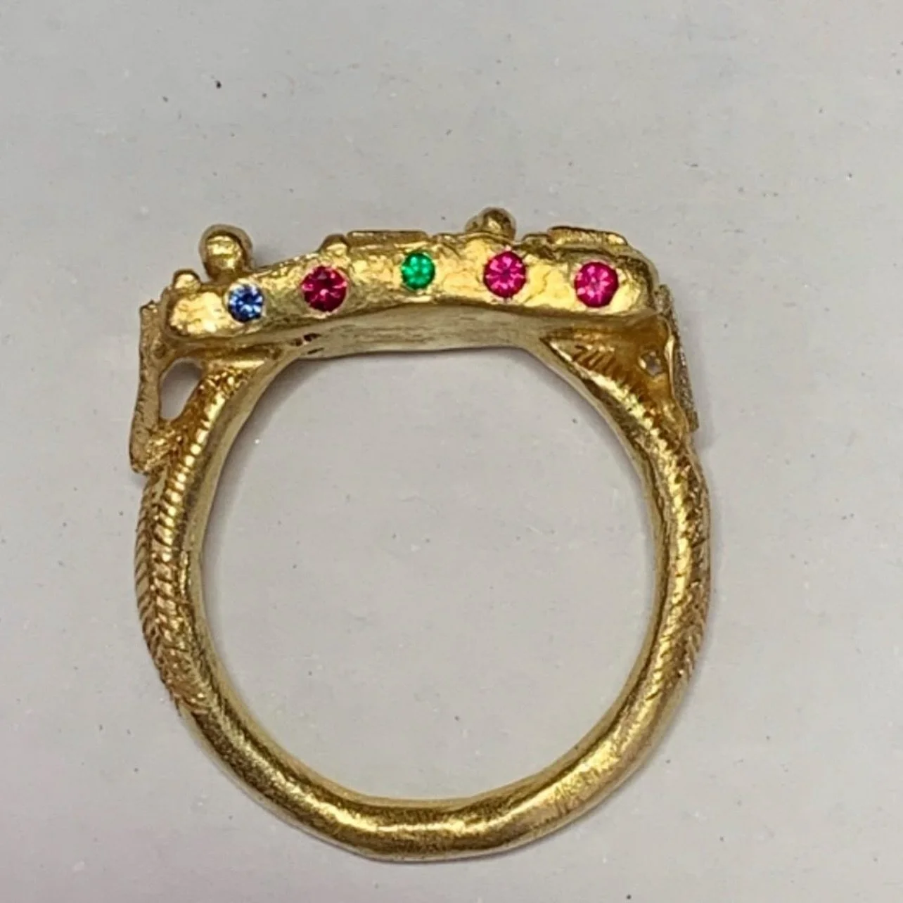 18ct yellow gold Symbols Signs and Script ring set with rubies, emerald, sapphire and diamond (set on top).

These precious elements are set in the side for the wearer of the ring. Flashes of colour appear when the hand moves.
There is a fashion for 