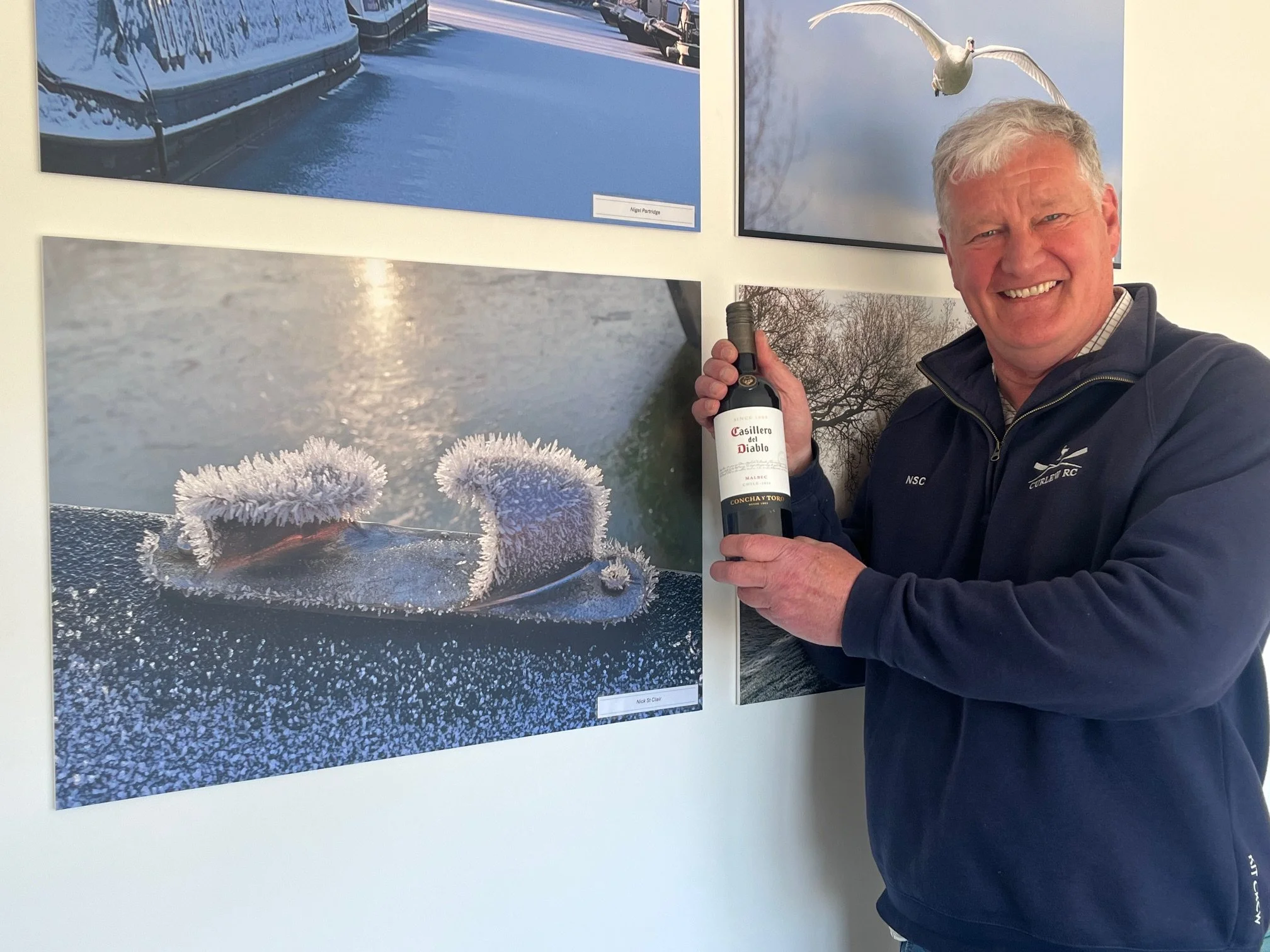 Smiling man with a bottle of red wine next to his winter cleats photograph