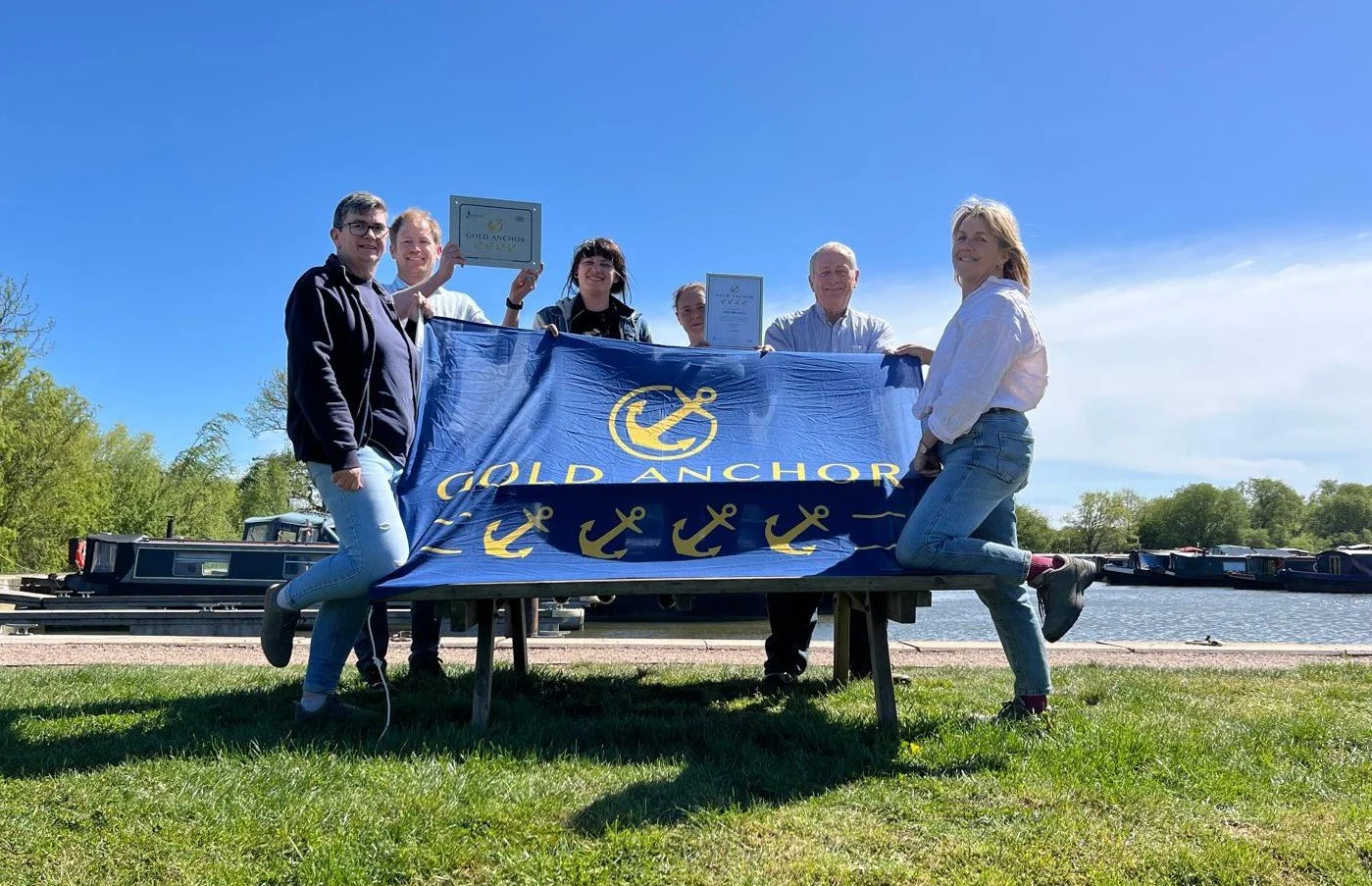 SIX TEAM MEMBERS DISPLAY LARGE BLUE GOLD ANCHORS FLAG ALONG WITH A CERTIFICATE AND PLAQ