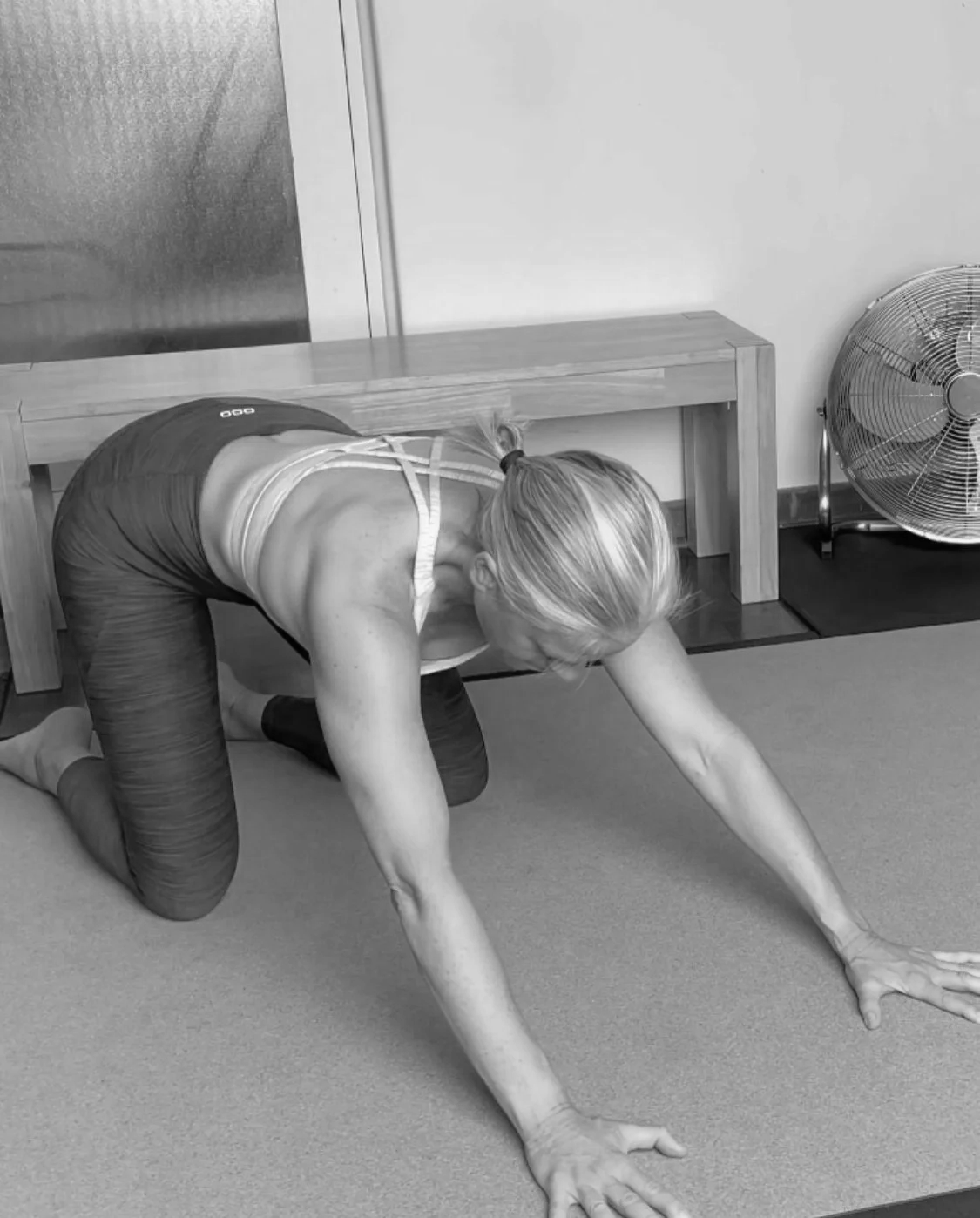 A woman in a kneeling position on the ground with hands on the ground rocking back into her hips for hip mobility in a mobility program for menopause.