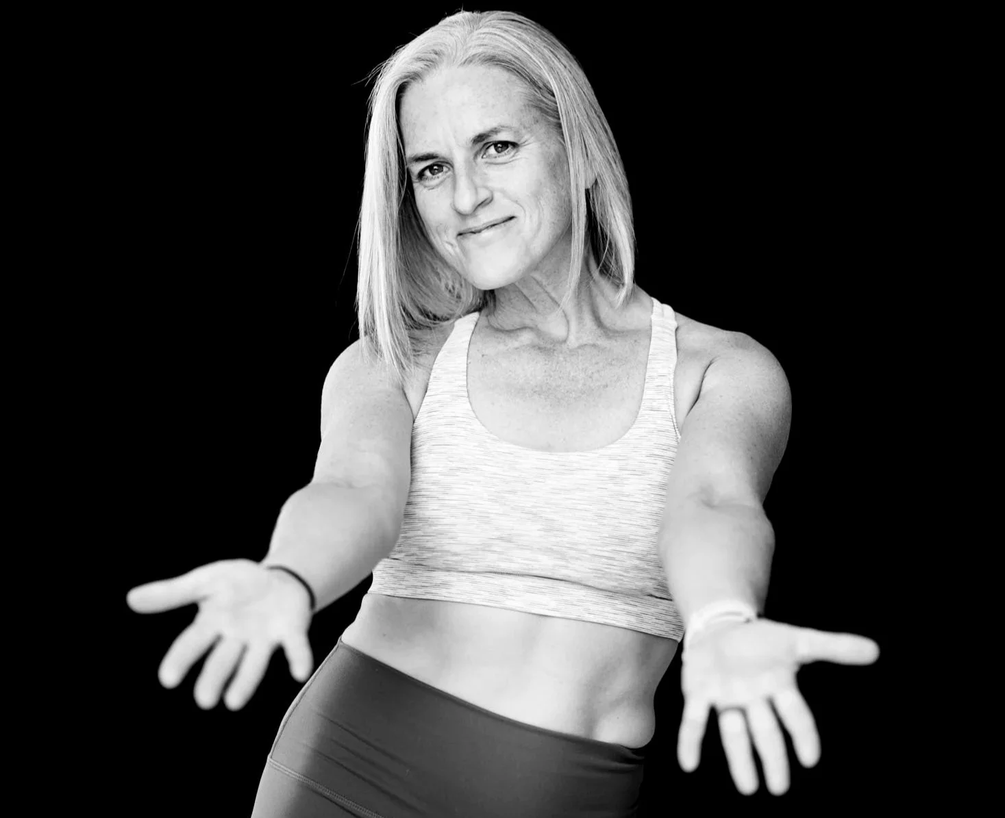 a personal trainer in Adelaide in a crop top and workout shorts smiling with arms open in an inviting gesture