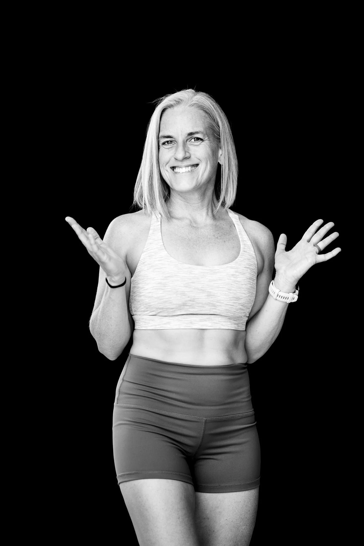 a woman in strength training clothes with arms open and a smile in an inviting pose