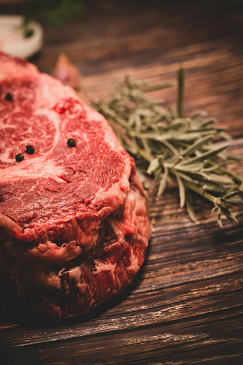 Raw bone-in rib roast with rosemary and seasoning on wooden surface
