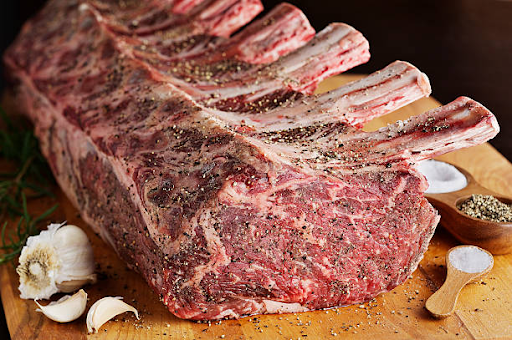 Bone-in rib roast seasoned with herbs and garlic on a cutting board