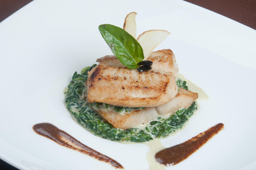 Pan-seared cod fillet served with greens and sauce on a plate