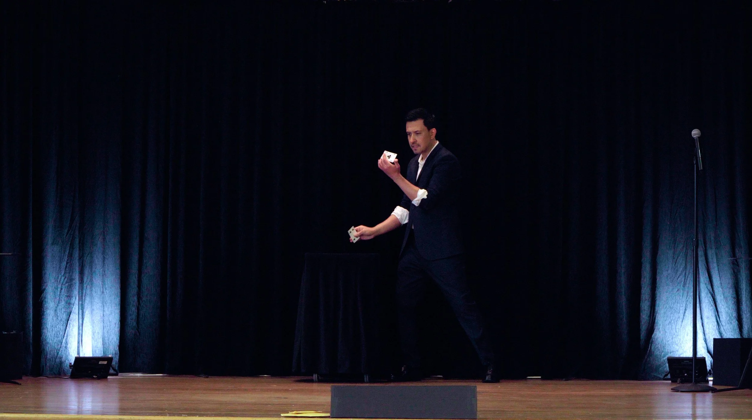 Christopher Moro performing card manipulation on a theater stage in Los Angeles, with dramatic uplighting and dark backdrop