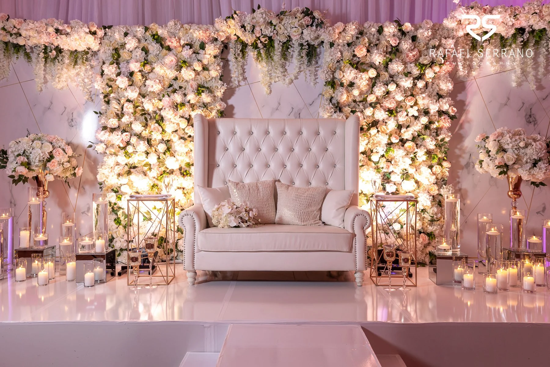 Wedding reception decor with candlelight, floral arrangements, and pink ambient lighting.