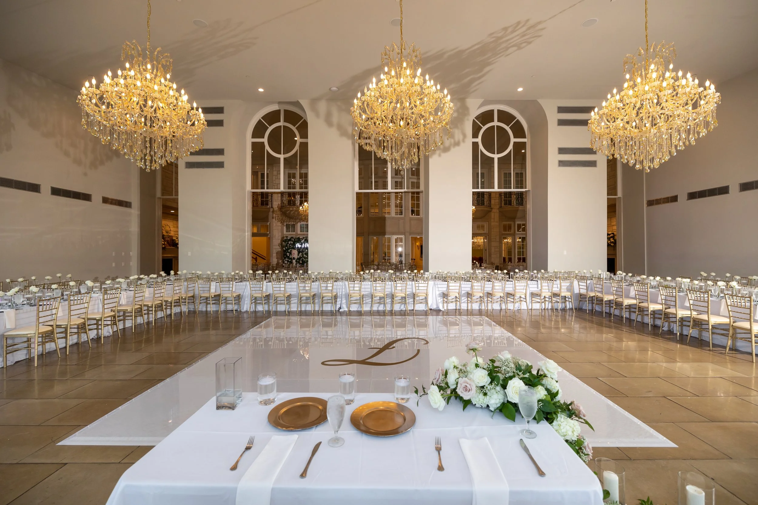 Elegant wedding reception with white decor, gold details, floral arrangements, and crystal chandeliers.