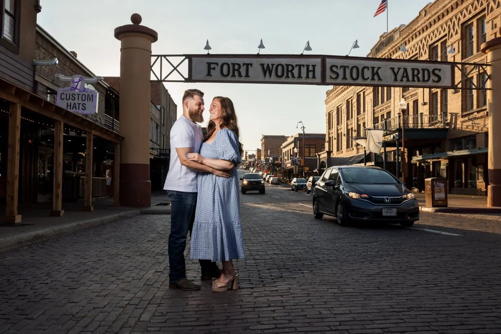 Lacey and Trey beneath the Fort Worth Stockyards sign with vehicles in the background.