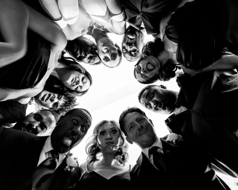 Black-and-white photograph looking up at the wedding party leaning toward the camera.