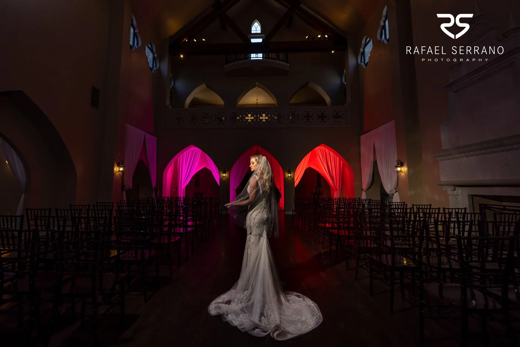 Bride wearing an elegant fitted wedding dress inside a dramatic ceremony space.